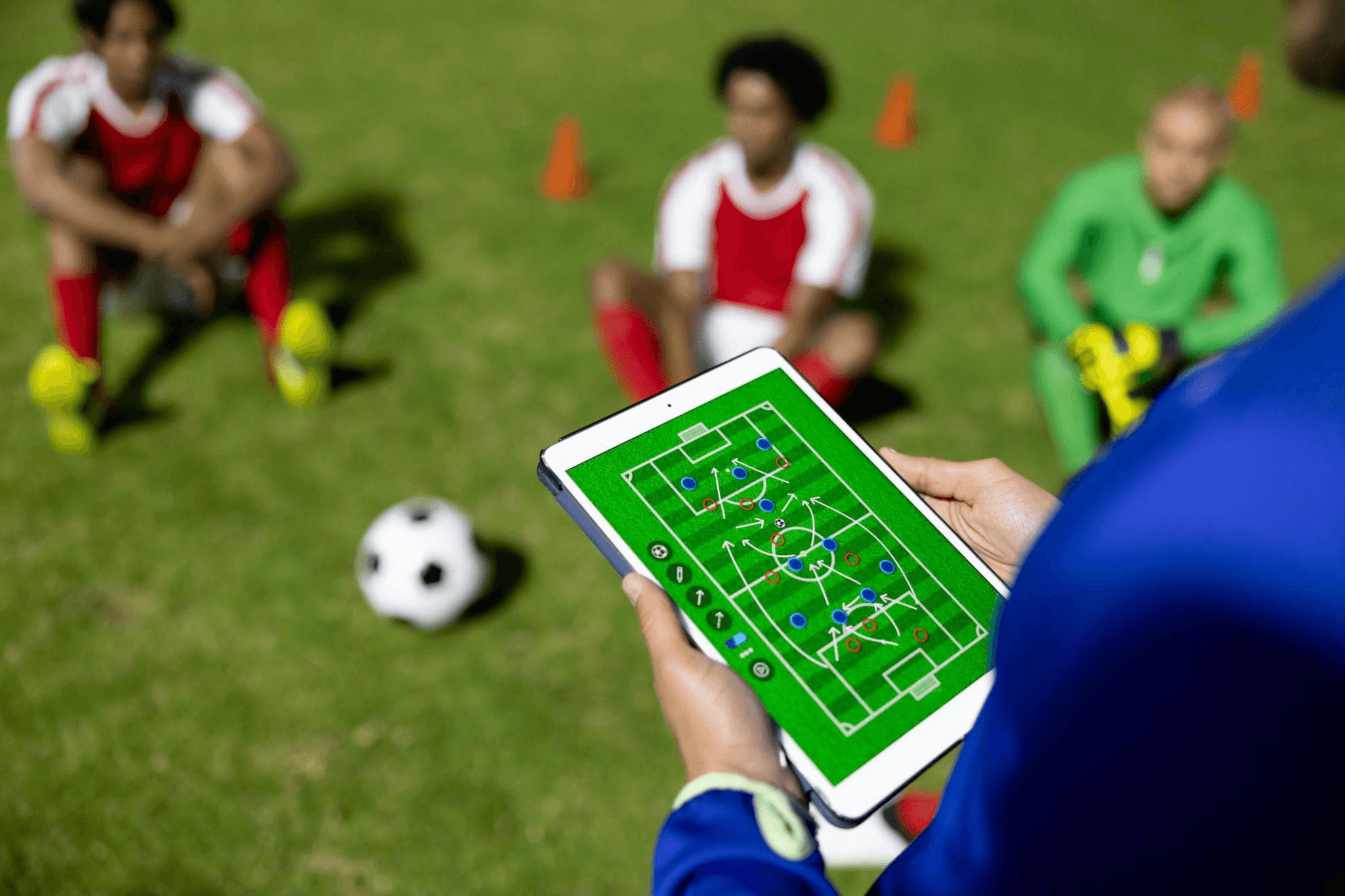 Coach reviewing post-match tactics on a tablet with players seated on the pitch